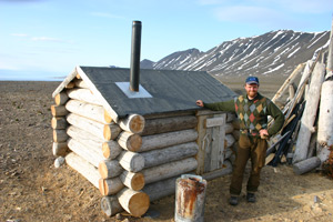 Jon Grande Dahl standing in front of a small wooden sauna. 